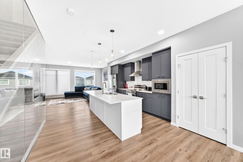 Open concept living area featuring wood-finish flooring, a white kitchen island, dark gray cabinetry, stainless steel appliances, and large windows - 479 39 St Sw, Edmonton, AB 