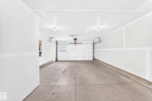 Attached two-car garage featuring a concrete floor, white interior walls, and an automatic garage door opener - 479 39 St Sw, Edmonton, AB 