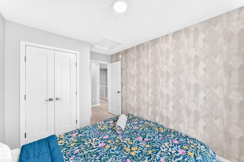 Room featuring a geometric patterned accent wall, white flat-panel closet doors with chrome hardware, an overhead flush-mount light, and light-colored carpeting - 479 39 St Sw, Edmonton, AB 