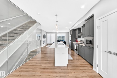 Wood-finish flooring throughout, kitchen featuring gray cabinetry, stainless steel appliances, and a central island with a waterfall countertop - 479 39 St Sw, Edmonton, AB 