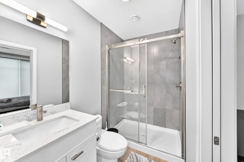 Modern bathroom featuring a vanity with a white countertop, a rectangular undermount sink, a large mirror, and an enclosed shower with a sliding glass door - 479 39 St Sw, Edmonton, AB 