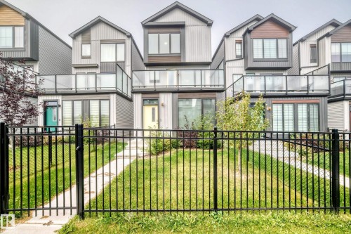 Modern exterior with multiple balconies featuring clear glass railings, a black metal fence, and a concrete pathway - 479 39 St Sw, Edmonton, AB 