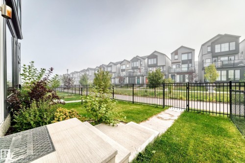 Concrete steps leading to a manicured lawn, established landscaping, and a black wrought iron fence - 479 39 St Sw, Edmonton, AB 