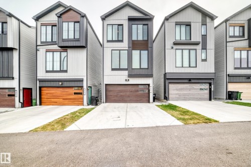 Contemporary exterior with vertical siding, dark trim accents, multiple windows, and a wood-finish garage door - 479 39 St Sw, Edmonton, AB 