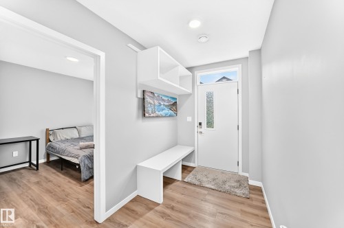 Entryway with wood-finish flooring, built-in shelving, built-in bench, recessed lighting, and a white entry door with a privacy glass insert - 479 39 St Sw, Edmonton, AB 