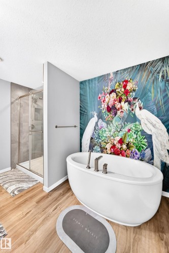 Freestanding soaking tub with polished chrome fixtures, wood-finish flooring, glass-enclosed shower, and decorative wall mural - 479 39 St Sw, Edmonton, AB 