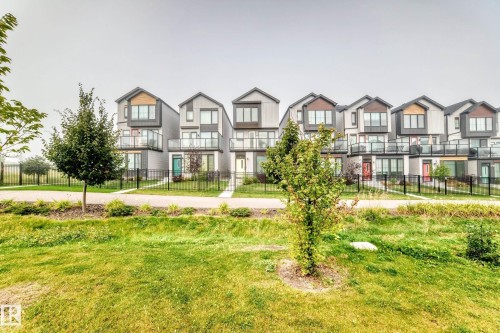 Modern townhomes featuring grey siding, dark trim accents, private balconies with glass railings, and individual front walkways - 479 39 St Sw, Edmonton, AB 