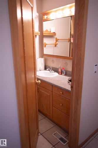 Ceramic tile flooring, wood-finish vanity with countertop, built-in sink, wall-mounted mirror, and vanity light fixture - 16503 68 Street Nw, Edmonton, AB 