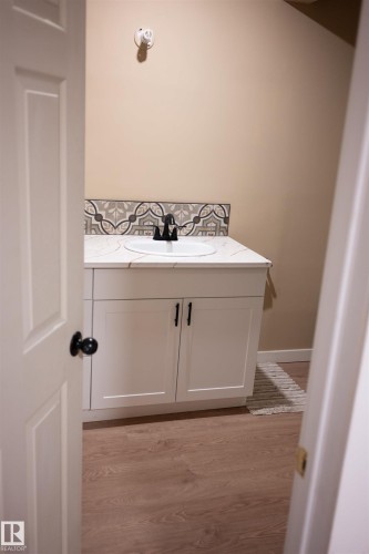 White vanity with white countertop, integrated sink, black faucet, and patterned tile backsplash - 16503 68 Street Nw, Edmonton, AB 