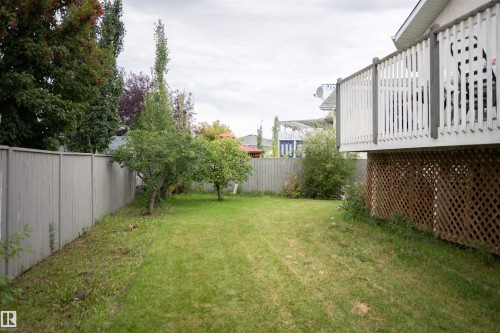 Expansive green space featuring a wooden privacy fence, mature trees, and a raised wooden deck with lattice skirting - 16503 68 Street Nw, Edmonton, AB 