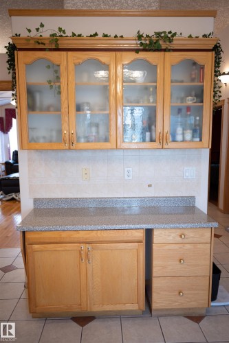 Wood-finish cabinetry with frosted glass inserts, speckled countertop, and tiled backsplash - 16503 68 Street Nw, Edmonton, AB 