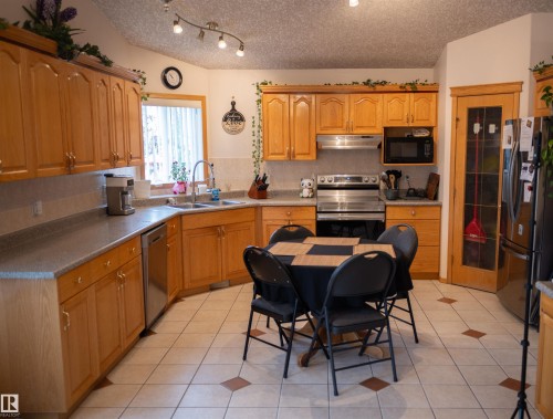 Full kitchen featuring wood-finish cabinetry, stainless steel appliances, a double basin sink, and tile flooring with accent squares - 16503 68 Street Nw, Edmonton, AB 