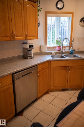 Wood-finish cabinetry, stainless steel dishwasher, dual basin sink with gooseneck faucet, tiled flooring, and a large window - 16503 68 Street Nw, Edmonton, AB 