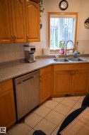 Wood-finish cabinetry, stainless steel dishwasher, dual basin sink with gooseneck faucet, tiled flooring, and a large window - 