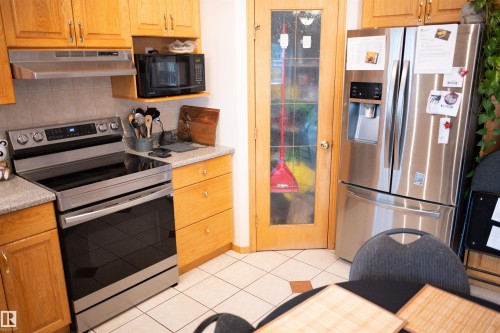 Stainless steel range, stainless steel French door refrigerator, wood-finish cabinetry, tile flooring, and frosted glass paneled door - 16503 68 Street Nw, Edmonton, AB 