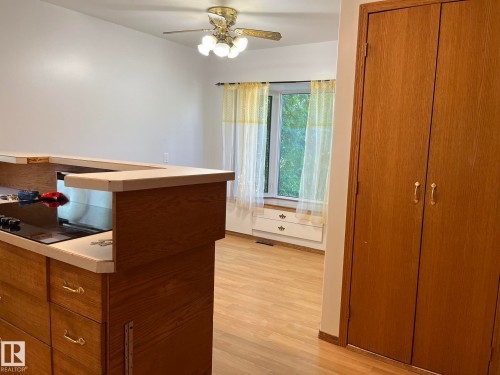 Built-in cooktop within a peninsula with wood-finish cabinetry, hard surface countertops, wood-finish flooring, ceiling fan with light fixture, and a built-in window seat with storage - 9504 63 Avenue Nw, Edmonton, AB 