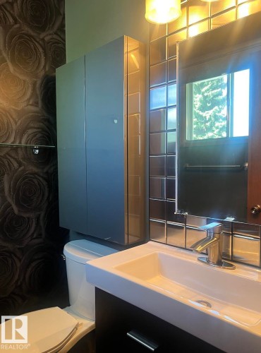 Powder room featuring a wall-mounted vanity with integrated sink, sleek wall-mounted storage cabinet, square metallic tile accent wall, and contemporary floral wallpaper - 15003 81 Street Nw, Edmonton, AB 