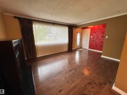 Wood-finish flooring, ample natural light from a large window, decorative red accent wall, and a front entry door with an oval glass insert - 
