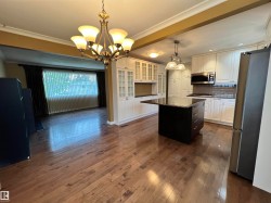 Wood-finish flooring throughout, kitchen island with dark finish and integrated storage, white cabinetry with glass-front uppers, stainless steel appliances, and a chandelier with frosted glass shades - 