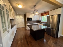 Spacious kitchen featuring white cabinetry, dark wood-finish flooring, stainless steel appliances, a center island with a dark countertop, and a tiled backsplash - 