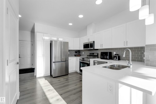 Modern kitchen featuring white cabinetry, stainless steel appliances, a white countertop, a tile backsplash, and wood-finish flooring - #62 2710 66 St Sw, Edmonton, AB 