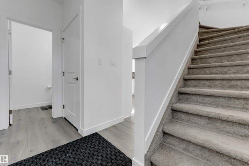 Hardwood-style flooring, white paneled doors, and carpeted stairs with a white railing - #62 2710 66 St Sw, Edmonton, AB 