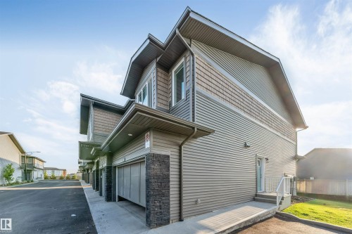 Modern townhouse exterior featuring horizontal siding, decorative shingle accents, black-trimmed windows, a garage door, and a private rear entrance with stairs - #62 2710 66 St Sw, Edmonton, AB 