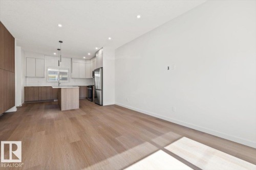 Open-concept living area featuring wood-finish flooring, recessed lighting, and a modern kitchen with a center island and stainless steel appliances - 15020 90 Avenue Northwest, Edmonton, AB 