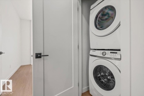 Stacked washer and dryer unit, wood-finish flooring, and minimalist interior doors with matte black hardware - 15020 90 Avenue Northwest, Edmonton, AB 