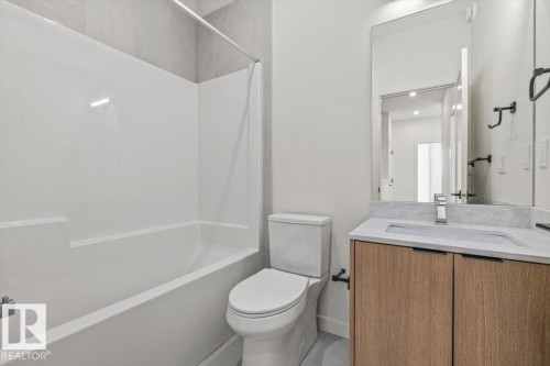 Bathroom featuring a built-in tub with shower, wood-finish vanity with an integrated sink, and a large wall-mounted mirror - 15020 90 Avenue Northwest, Edmonton, AB 