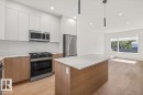 Kitchen featuring white upper cabinetry, wood-finish lower cabinetry, stainless steel appliances, a center island with a light-colored countertop, and recessed lighting - 15020 90 Avenue Northwest, Edmonton, AB 