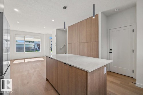 Kitchen island with a light-toned countertop, wood-finish cabinetry, and contemporary pendant lighting - 15020 90 Avenue Northwest, Edmonton, AB 