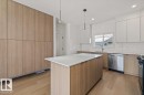 Modern kitchen featuring a large center island with a light-toned countertop, wood-finish cabinetry, stainless steel appliances, and sleek pendant lighting - 15020 90 Avenue Northwest, Edmonton, AB 