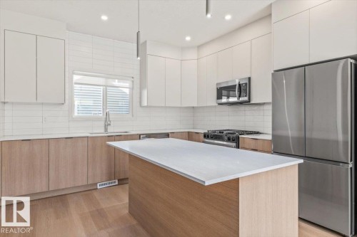 Kitchen featuring wood-finish flooring, two-tone cabinetry, stainless steel appliances, a center island with a light-toned countertop, and a tiled backsplash - 15020 90 Avenue Northwest, Edmonton, AB 