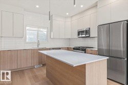 Kitchen featuring wood-finish flooring, two-tone cabinetry, stainless steel appliances, a center island with a light-toned countertop, and a tiled backsplash - 