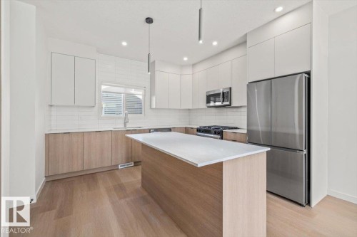 Kitchen featuring a central island, wood-finish flooring, white subway tile backsplash, and stainless steel appliances - 15020 90 Avenue Northwest, Edmonton, AB 