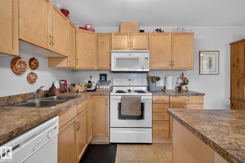 Full kitchen featuring wood-finish cabinetry, a double basin stainless steel sink, a white electric range, and a white microwave - #335 2096 Blackmud Creek Dr Sw, Edmonton, AB - Indoor Photo Showing Kitchen With Double Sink