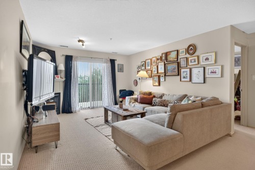 Spacious living area featuring neutral carpeting, light-toned walls, and a sliding glass door providing natural light - #335 2096 Blackmud Creek Dr Sw, Edmonton, AB - Indoor Photo Showing Living Room