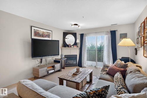 Living area featuring a corner fireplace with a mantel, a sliding glass door leading to a private balcony, track lighting, and neutral wall tones - #335 2096 Blackmud Creek Dr Sw, Edmonton, AB - Indoor Photo Showing Living Room With Fireplace