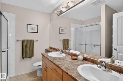 Bathroom with dual vanity featuring integrated sinks, light wood-finish cabinetry, and a full-width mirror - #335 2096 Blackmud Creek Dr Sw, Edmonton, AB - Indoor Photo Showing Bathroom