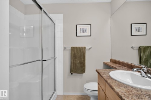 Bathroom featuring a sliding glass shower enclosure, beige wall paint, a light wood vanity with a speckled countertop, a drop-in sink, and a large wall-mounted mirror - #335 2096 Blackmud Creek Dr Sw, Edmonton, AB - Indoor Photo Showing Bathroom