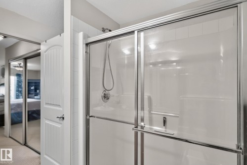 Shower enclosure featuring a sliding glass door and a wall-mounted showerhead with a handheld sprayer - #335 2096 Blackmud Creek Dr Sw, Edmonton, AB - Indoor Photo Showing Bathroom