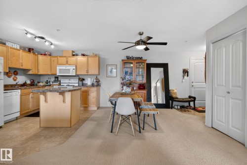 Open-concept living area featuring a kitchen with light wood cabinetry, stone-finish countertops, and white appliances - #335 2096 Blackmud Creek Dr Sw, Edmonton, AB - Indoor Photo Showing Kitchen