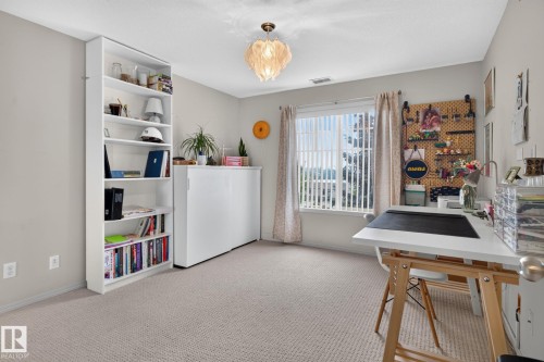 Carpeted room featuring a large window with vertical blinds, a built-in white bookshelf, and a decorative ceiling light fixture - #335 2096 Blackmud Creek Dr Sw, Edmonton, AB - Indoor