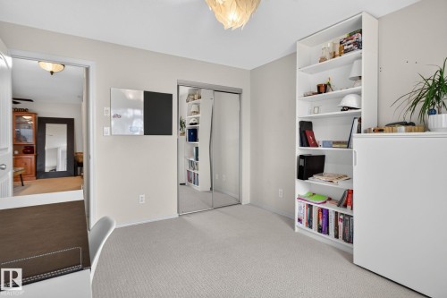 Neutral-toned room featuring a textile-finish carpet, white built-in shelving, and mirrored closet doors - #335 2096 Blackmud Creek Dr Sw, Edmonton, AB - Indoor