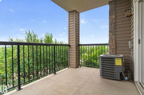 Private balcony featuring concrete flooring, black metal railings, and a stone veneer column - #335 2096 Blackmud Creek Dr Sw, Edmonton, AB - Outdoor With Exterior