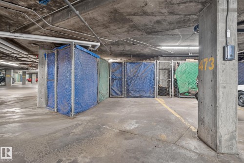 Concrete parking garage with exposed piping, fluorescent lighting, and designated storage units - #335 2096 Blackmud Creek Dr Sw, Edmonton, AB - Indoor