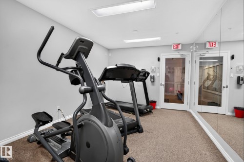 Fitness room featuring an elliptical machine, treadmill, mirrored wall, and carpet flooring - #335 2096 Blackmud Creek Dr Sw, Edmonton, AB - Indoor Photo Showing Gym Room