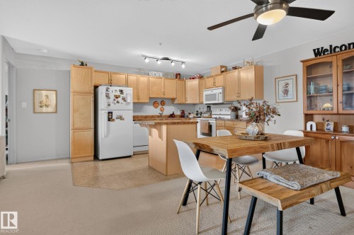 Kitchen and dining area featuring light wood-finish cabinetry, a built-in microwave, a ceiling fan with integrated lighting, a track lighting fixture, and a built-in hutch with glass-front display cabinets - #335 2096 Blackmud Creek Dr Sw, Edmonton, AB - Indoor