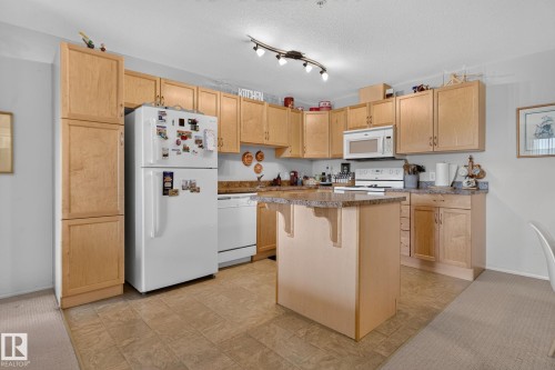 Kitchen featuring light wood cabinetry, a central island with a stone-finish countertop, and matching stone-finish perimeter countertops - #335 2096 Blackmud Creek Dr Sw, Edmonton, AB - Indoor Photo Showing Kitchen